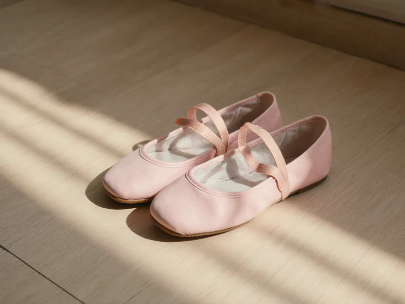 A pair of pink ballet shoes with crossed ribbon straps, on a pale timber floor